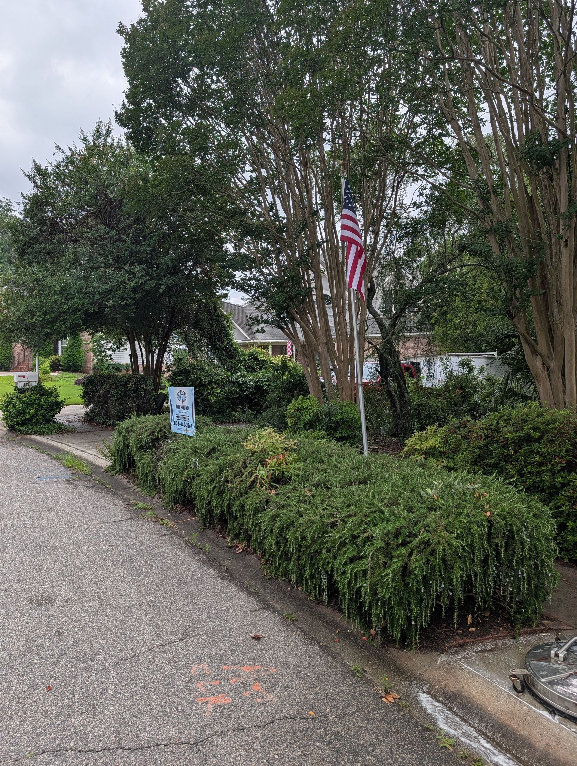 Gravel path beside trimmed hedges and trees, with an American flag hanging near a quiet garden area.
