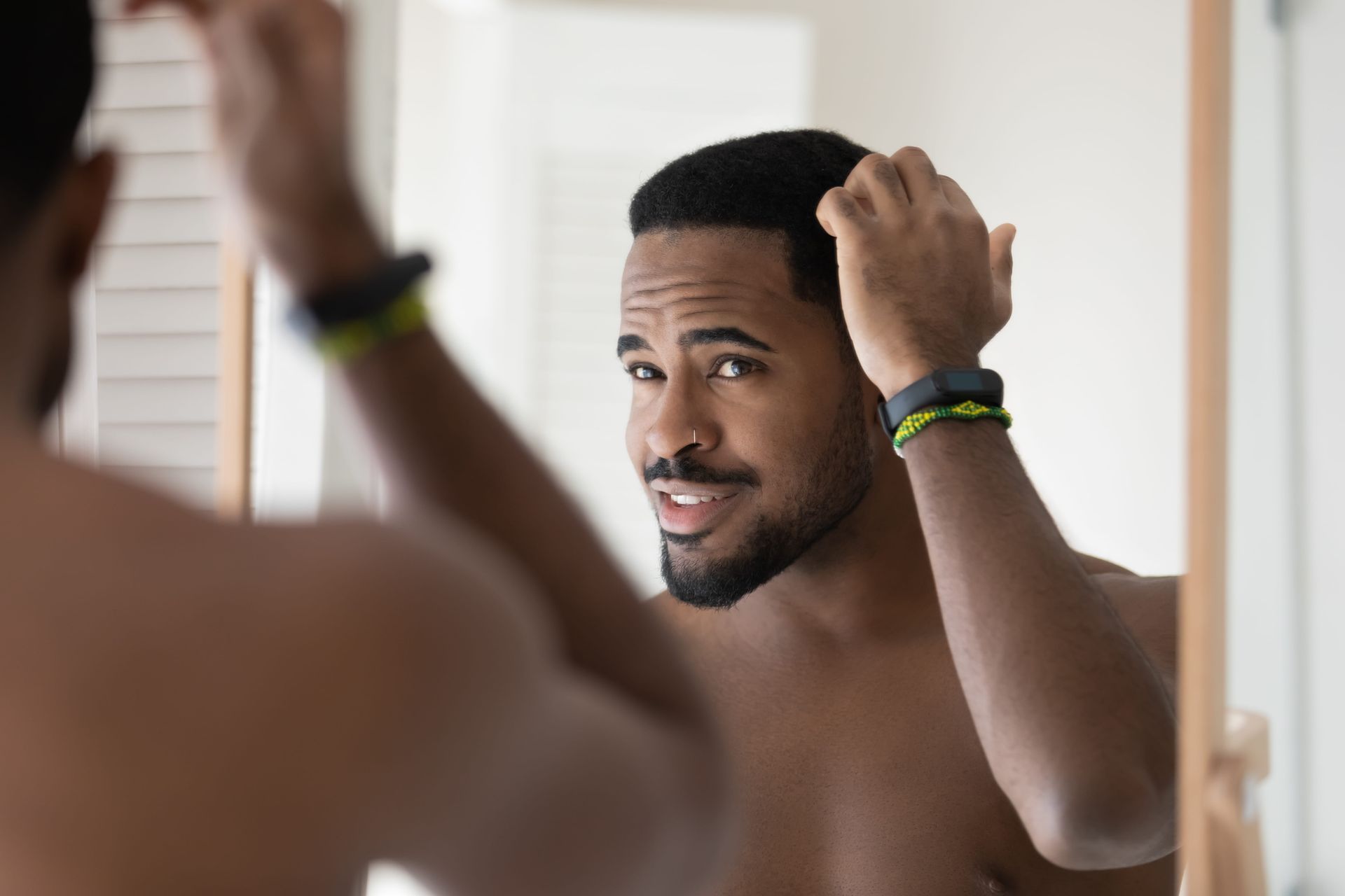 Man styling his hair in a bathroom mirror, wearing wristbands and smiling slightly