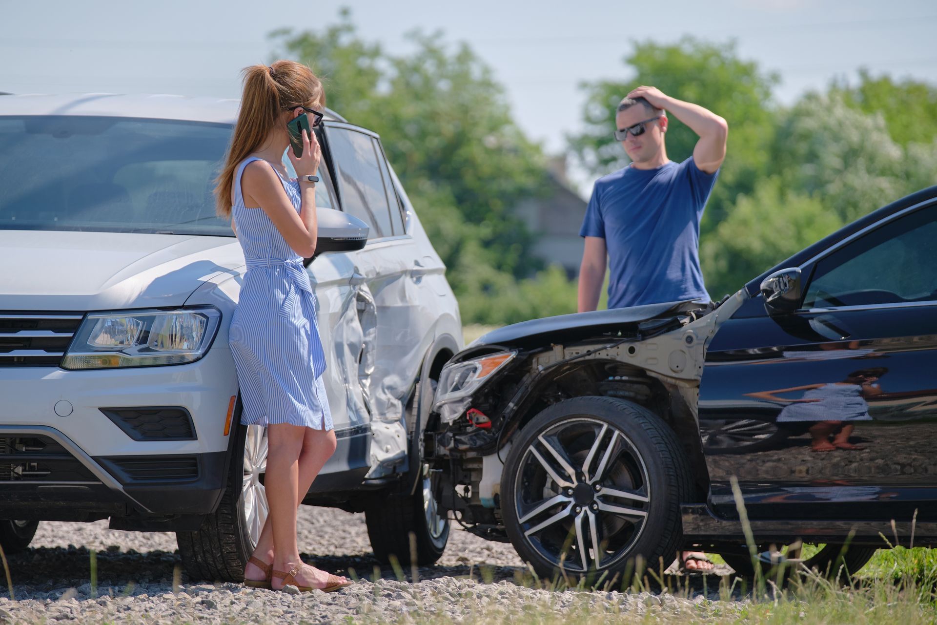 Two drivers stand beside two damaged cars after a collision on the roadside.