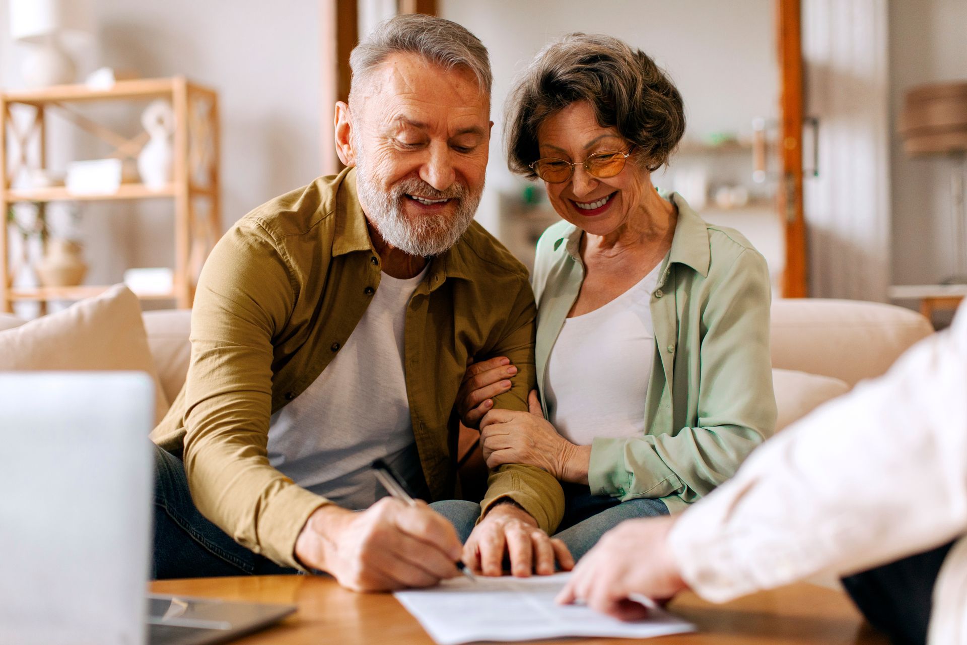 Couple smiling while signing papers at a desk in a bright living room