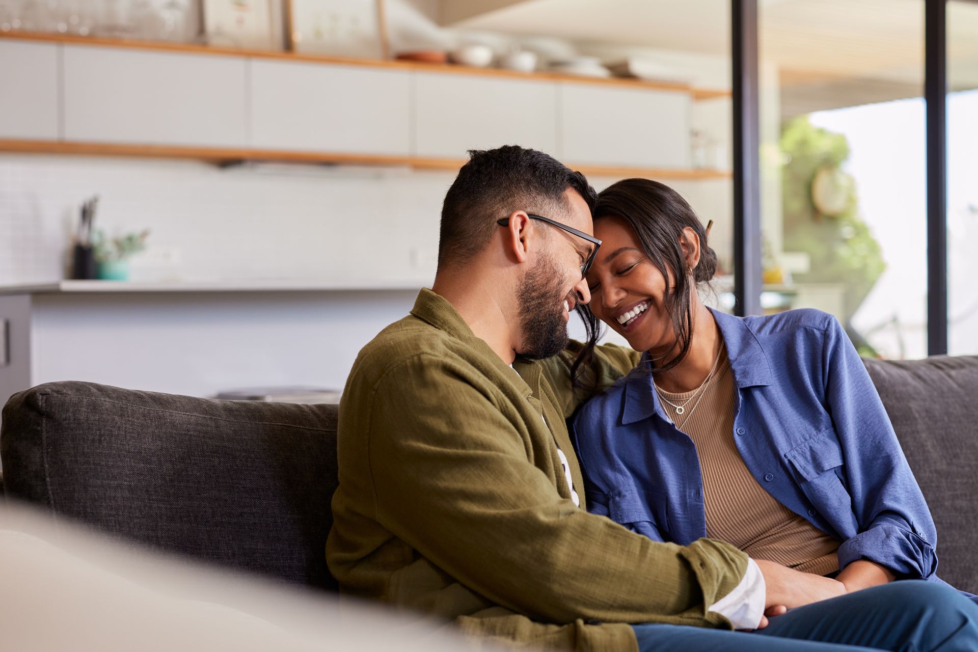 Two people smiling on a couch in a bright living room, leaning close together