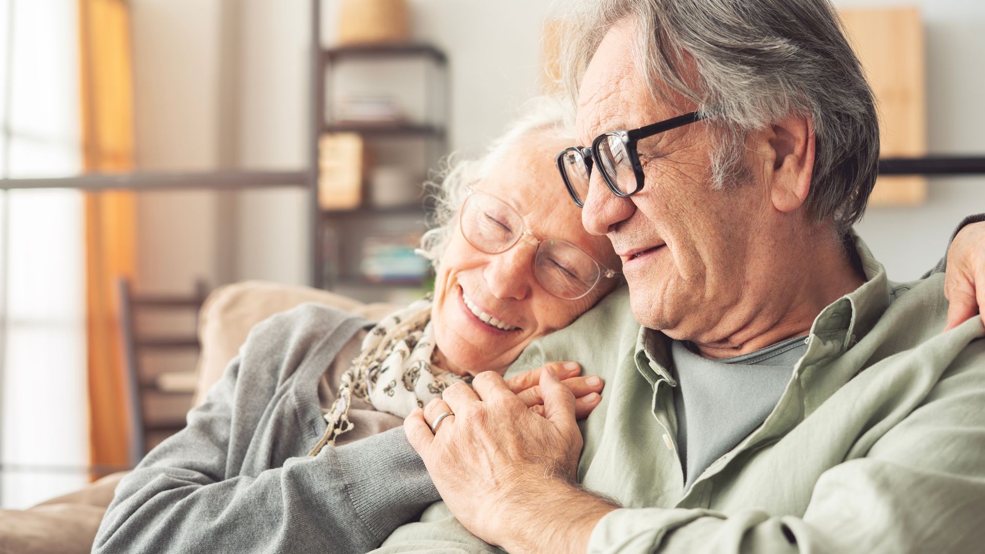 Two older adults smiling and cuddling on a couch in a cozy living room