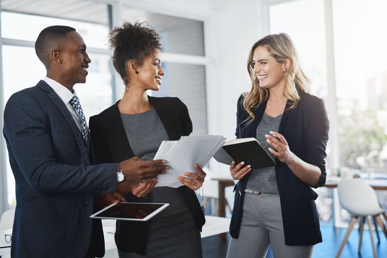 Three coworkers discussing documents in a bright office lobby