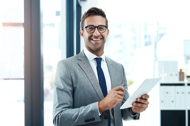 Smiling professional in gray suit holding a tablet and stylus in a bright office