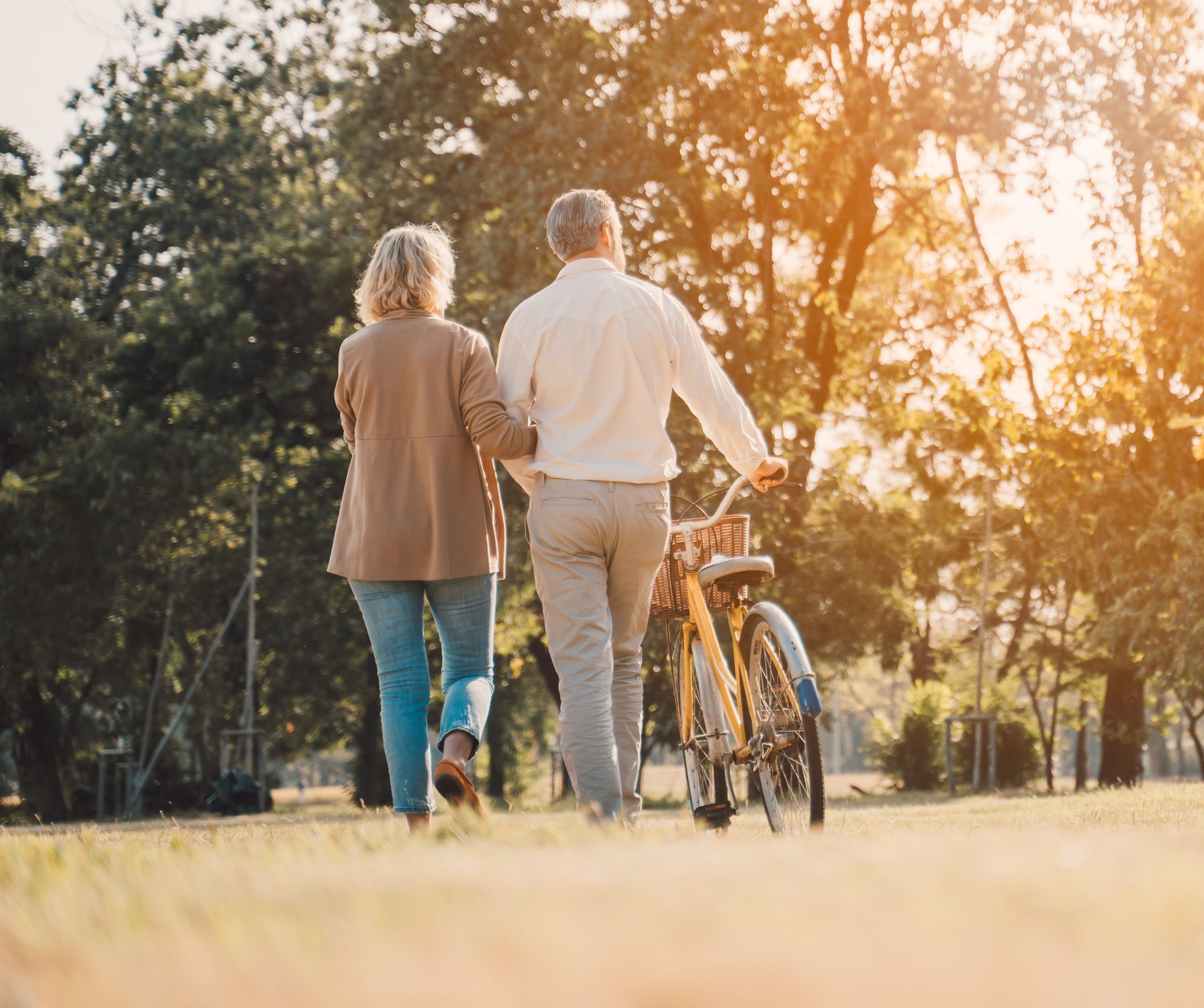 Two people walk beside a bicycle on a sunlit path at golden hour