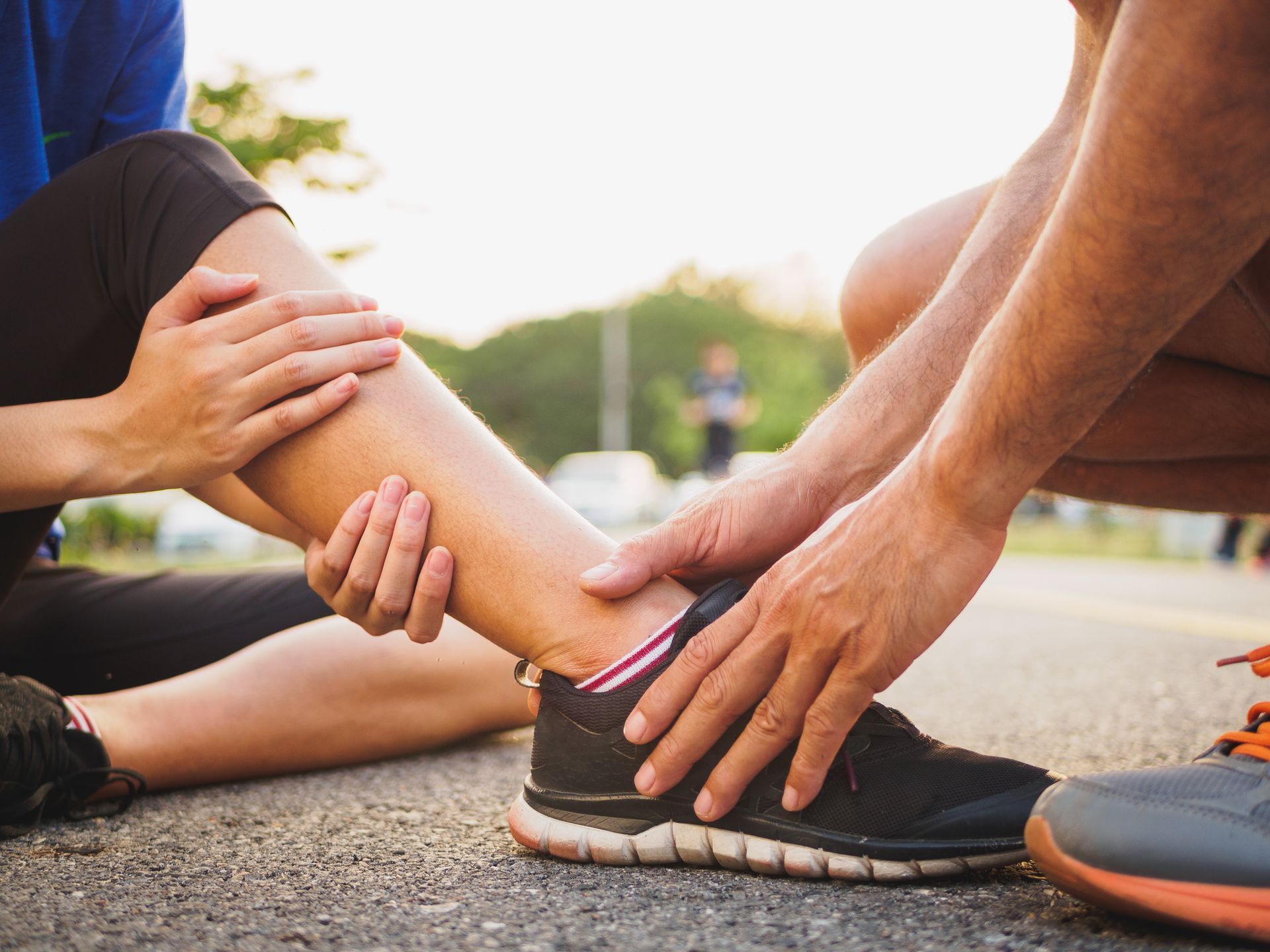 Person injured on road, receiving ankle support from another person wearing running shoes.