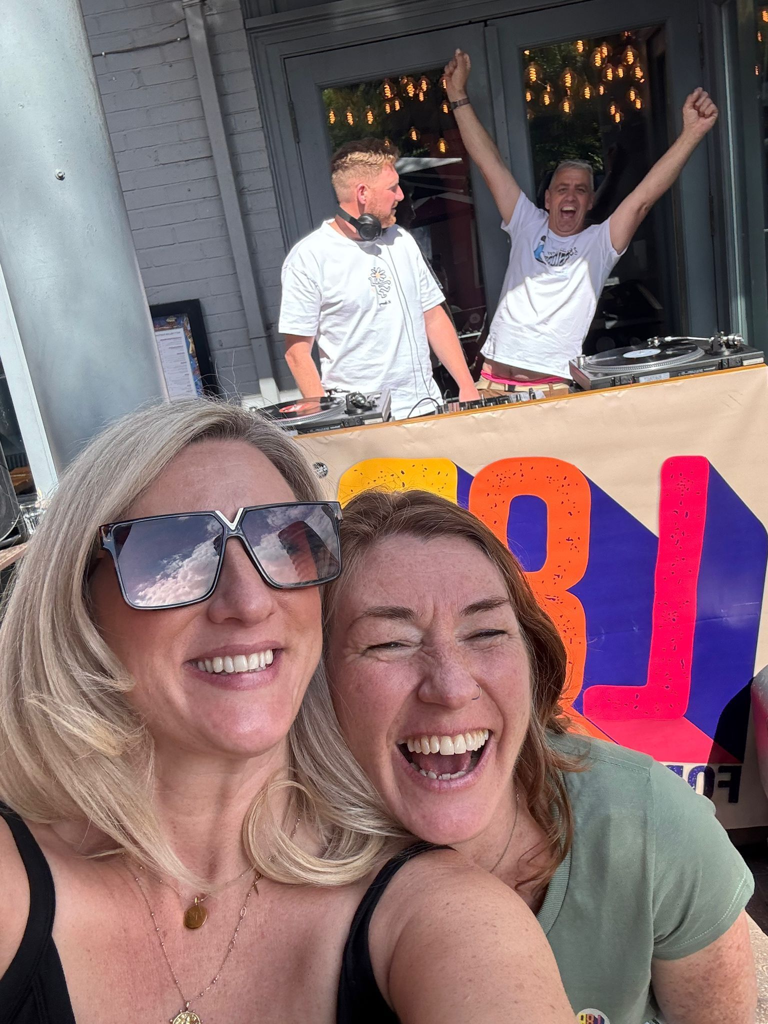 Two women are posing for a picture in front of a dj.