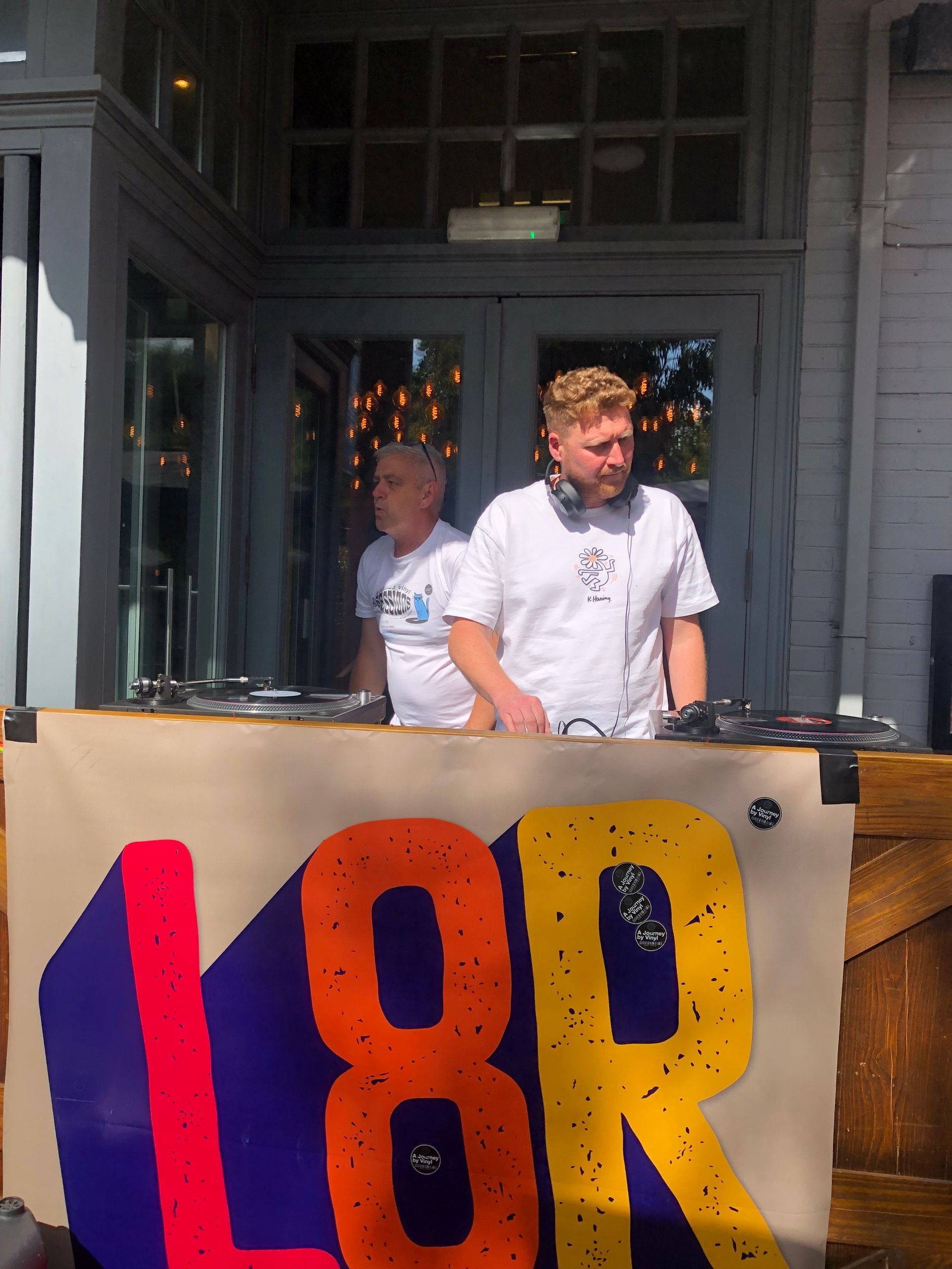 Two men are behind a table with a sign that says l8r