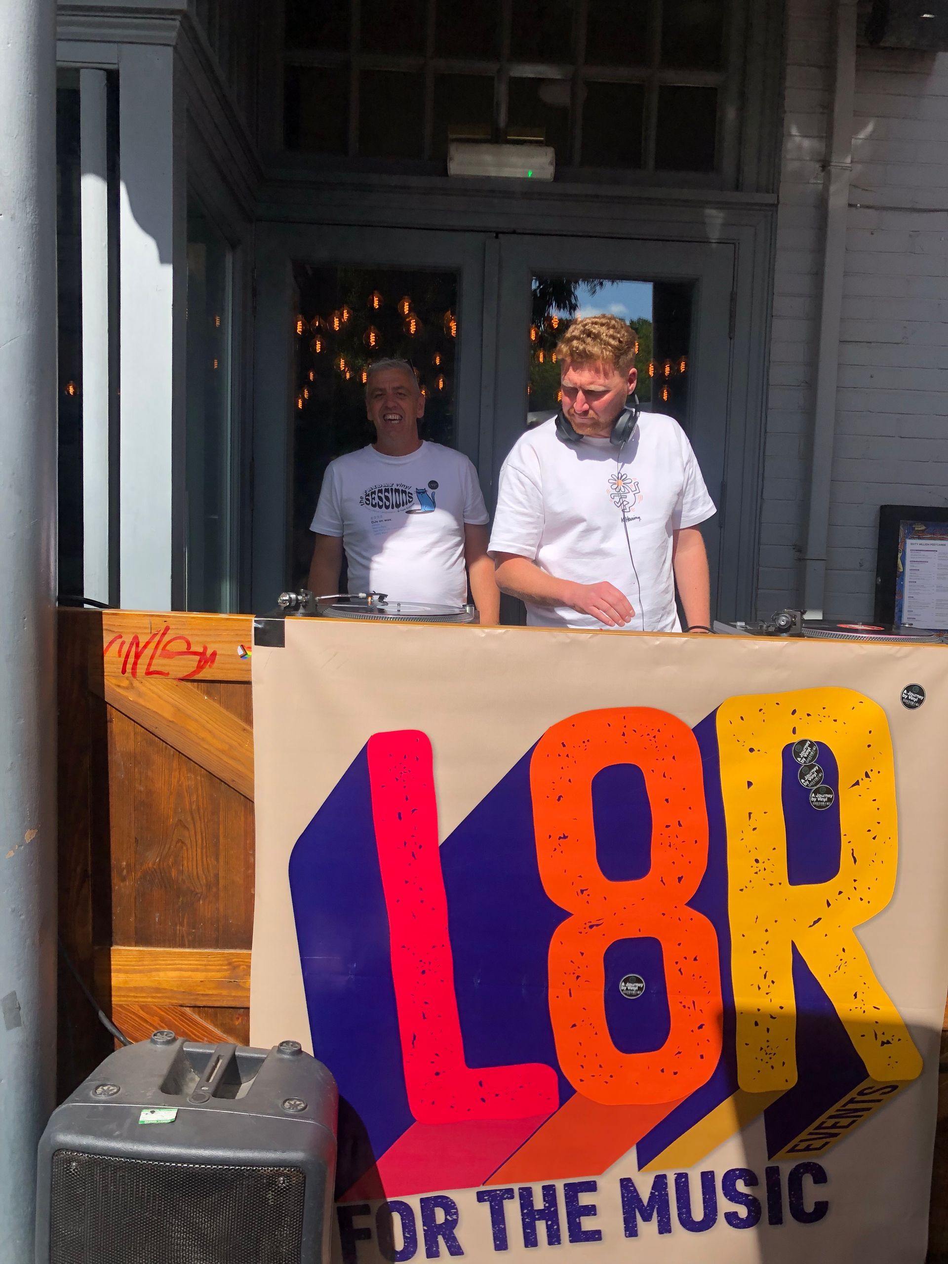 Two men are standing behind a sign that says l8r for the music
