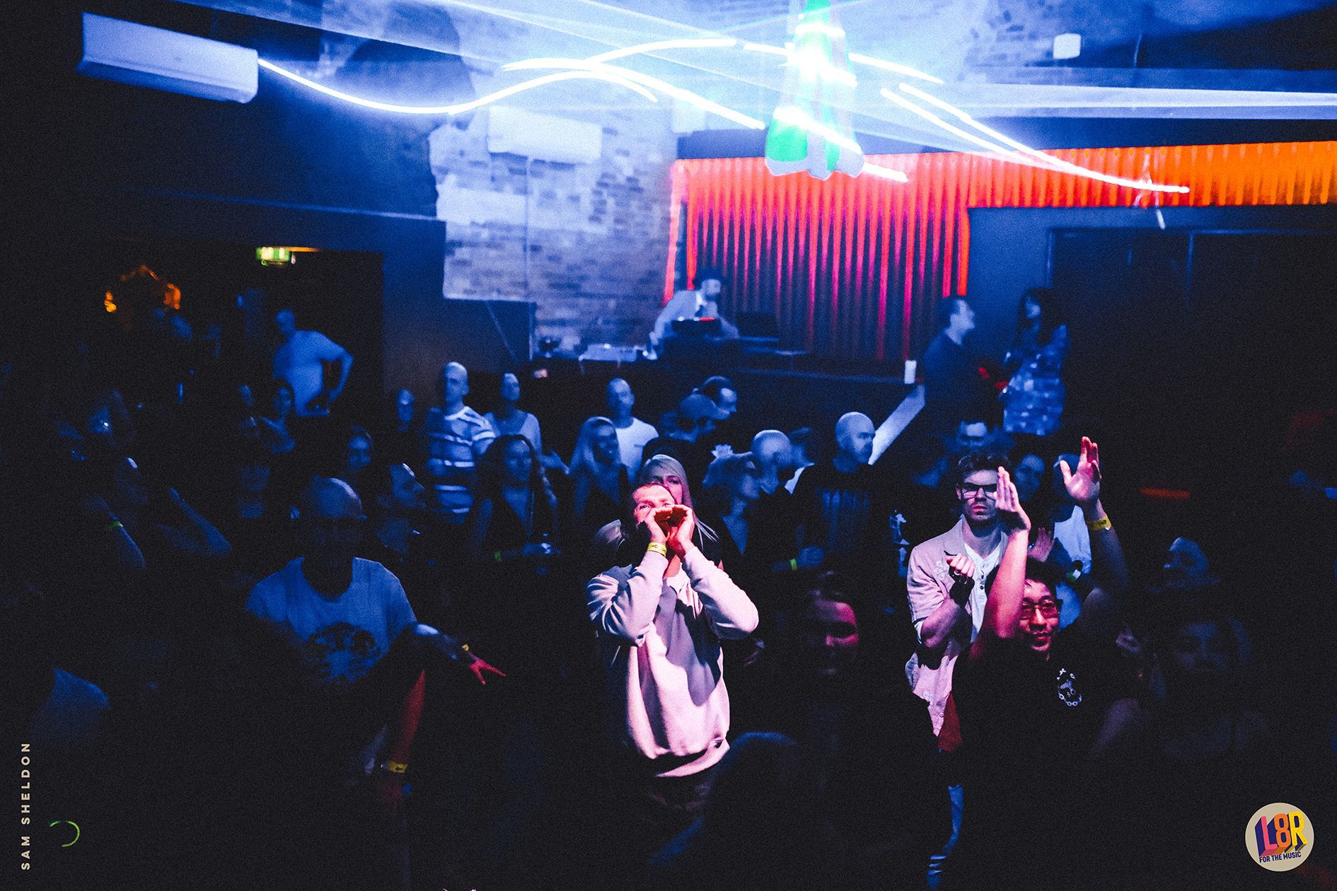 A crowd of people are standing in a dark room at a party.
