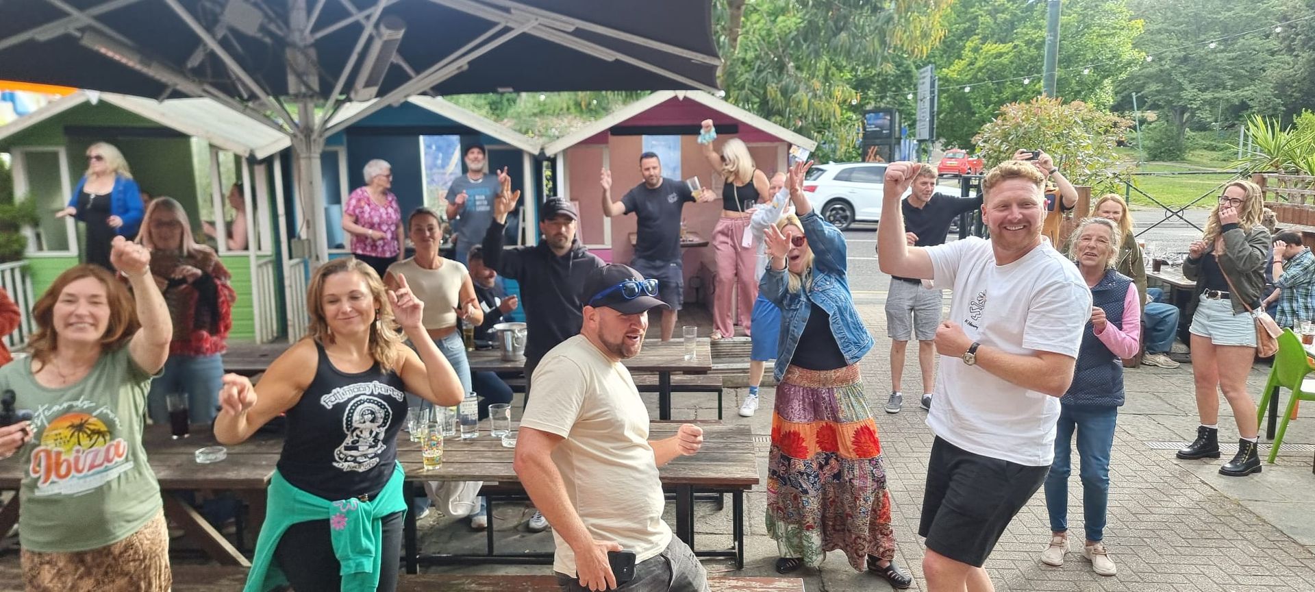 A group of people are standing in front of a picnic table under an umbrella.