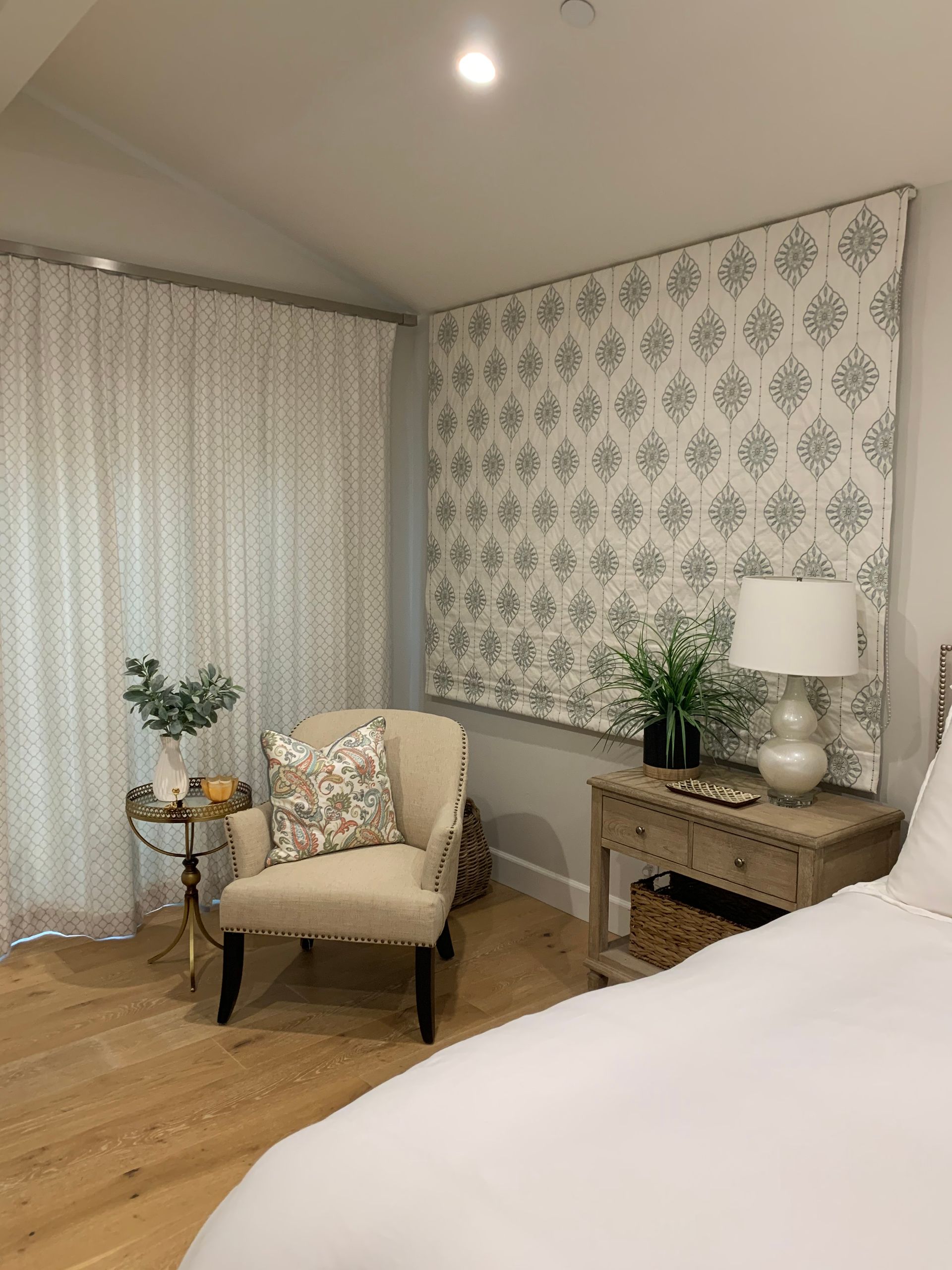 A bedroom with a bed , chair , nightstand and lamps.