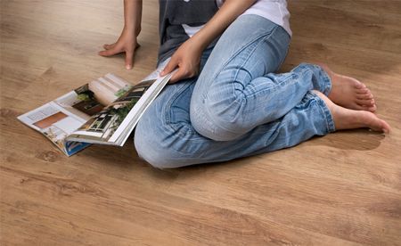 Persona en jeans, descalza, sentada en un piso de madera, leyendo una revista.