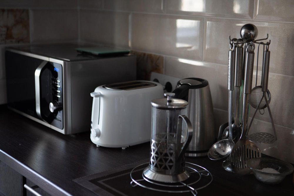 Encimera de cocina con microondas, tostadora, cafetera, hervidor y utensilios.