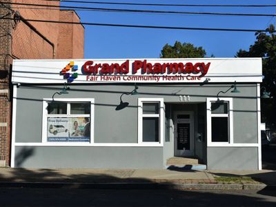 Grand Pharmacy storefront with gray facade, red sign, and colorful balloons outside