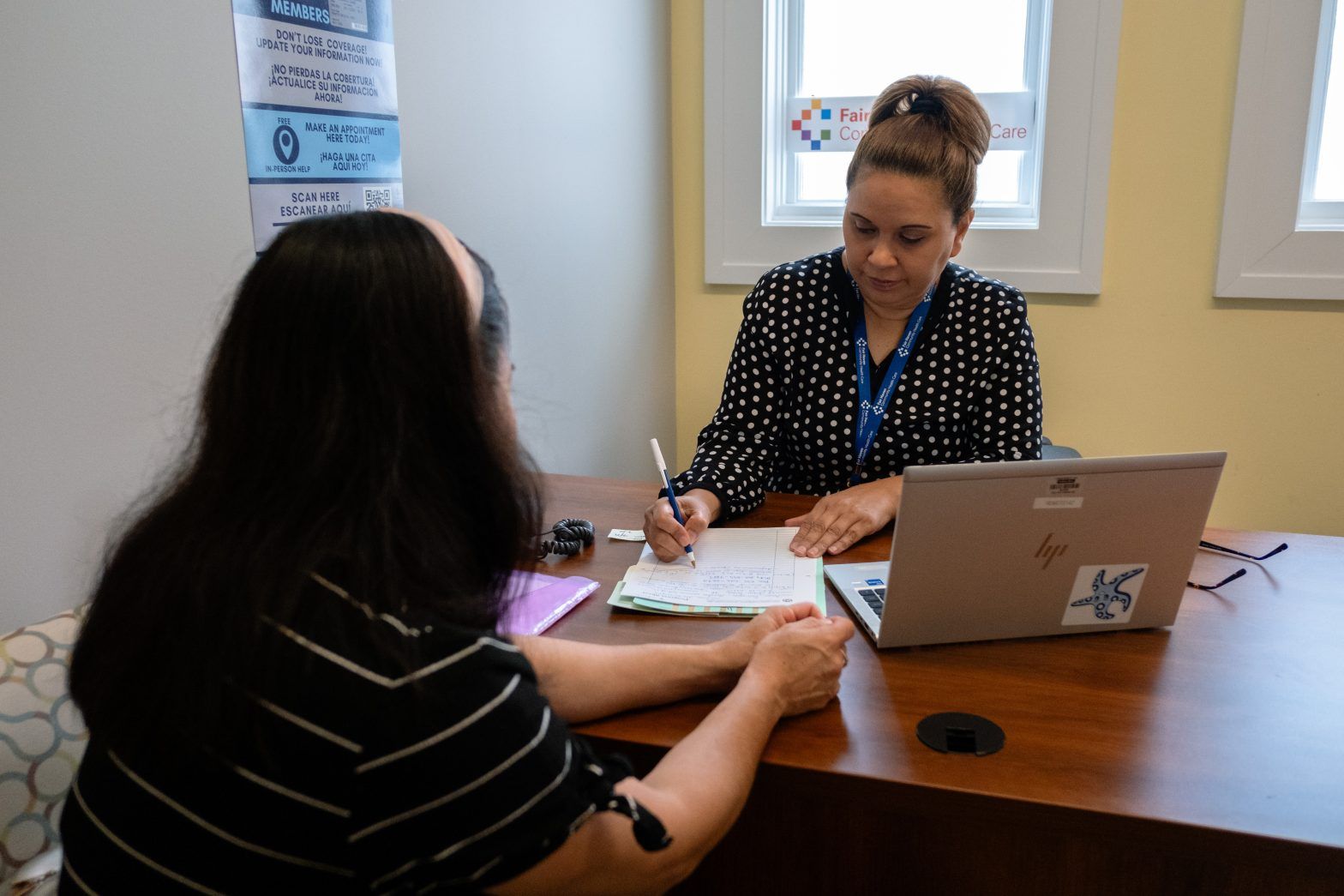 Two people seated at a desk, reviewing paperwork beside a laptop in a bright office.