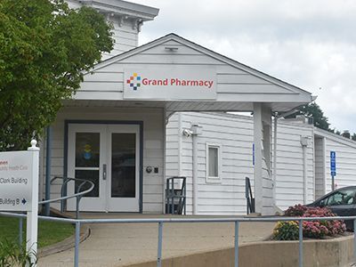 Grand Pharmacy storefront with gray facade, red sign, and colorful balloons outside