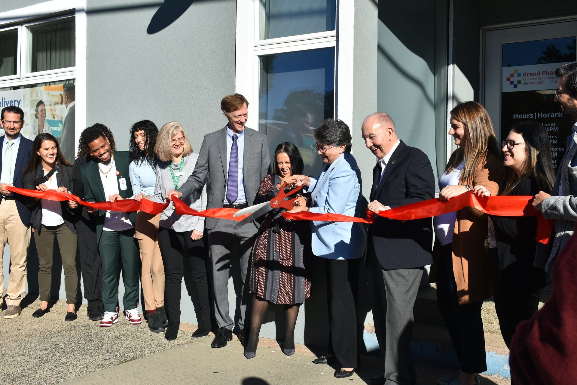 People cutting a red ribbon outside a building at a ribbon-cutting ceremony