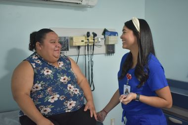 Two women talking in a clinic room, one holding a stethoscope and smiling.