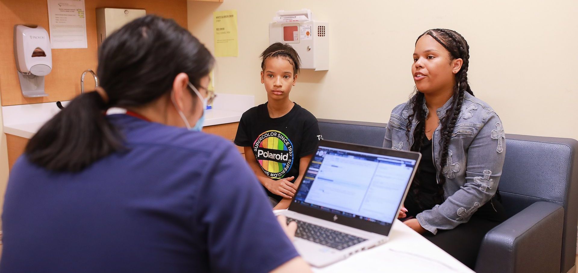 Two women meet with a counselor in an office, seated on a couch beside an open laptop.