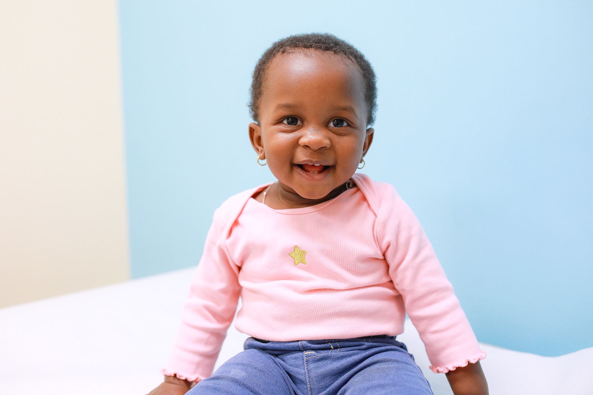 A smiling toddler sits on a white surface against a blue and beige wall
