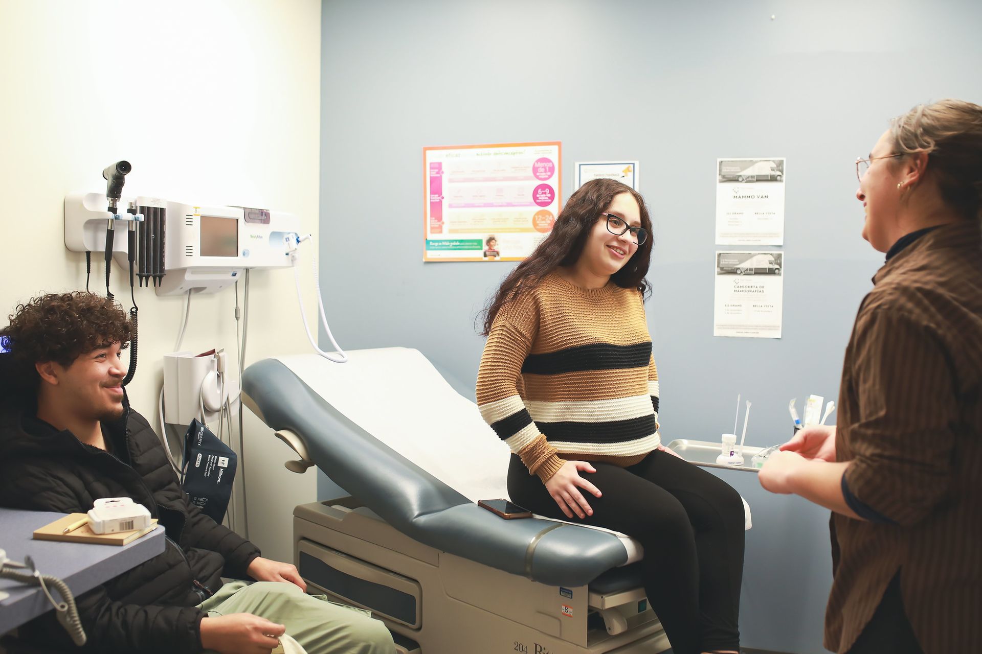 Patients and a clinician talking in an exam room with a medical chair and equipment