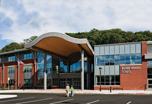 Modern school building with a curved roof and glass entrance, red brick wings, and a parking lot in front