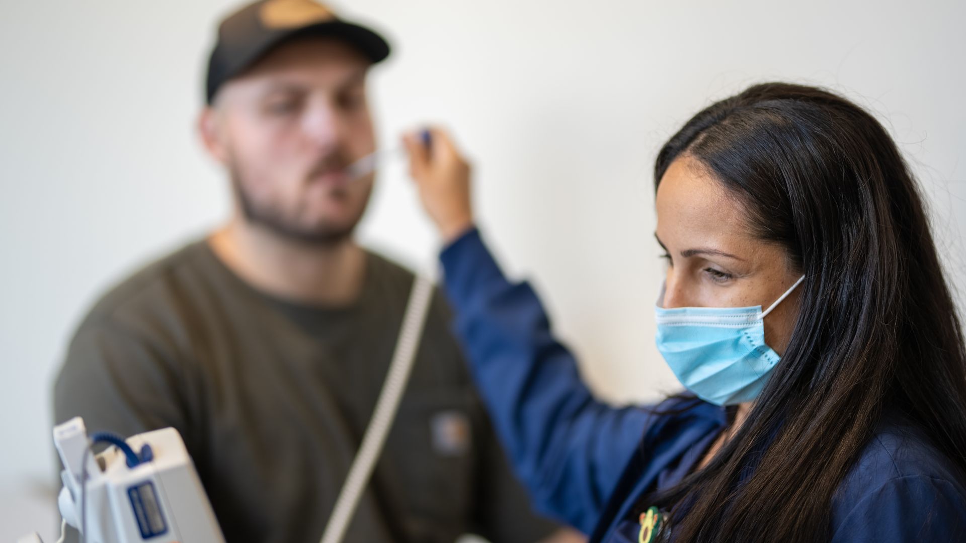 A healthcare worker in a face mask uses an oral thermometer to take a patient's temperature.