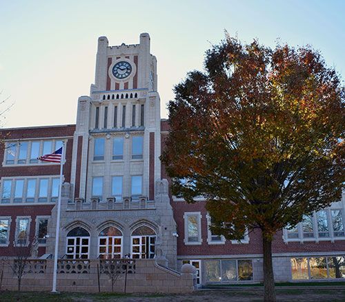 Historic brick school building with a clock tower and autumn tree in front
