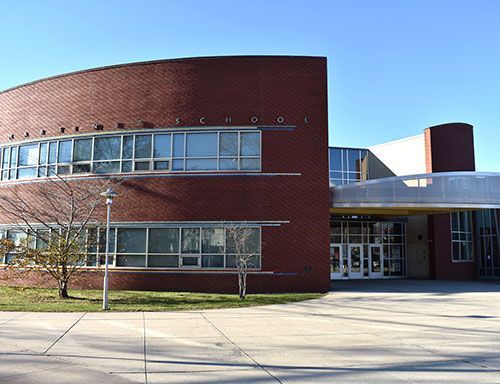 Modern brick building with curved facade, large windows, and main entrance under a clear blue sky