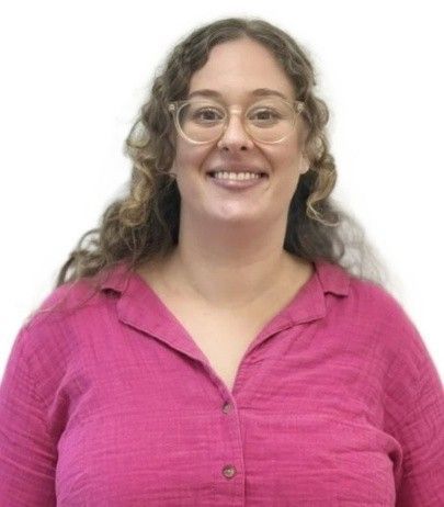 Smiling person with curly hair and glasses wearing a bright pink shirt against a white background