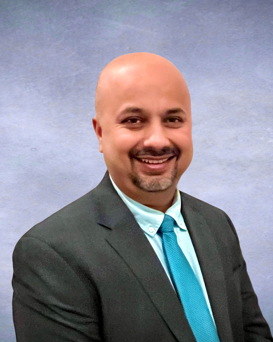 Smiling man in a dark suit and teal tie against a light gray background