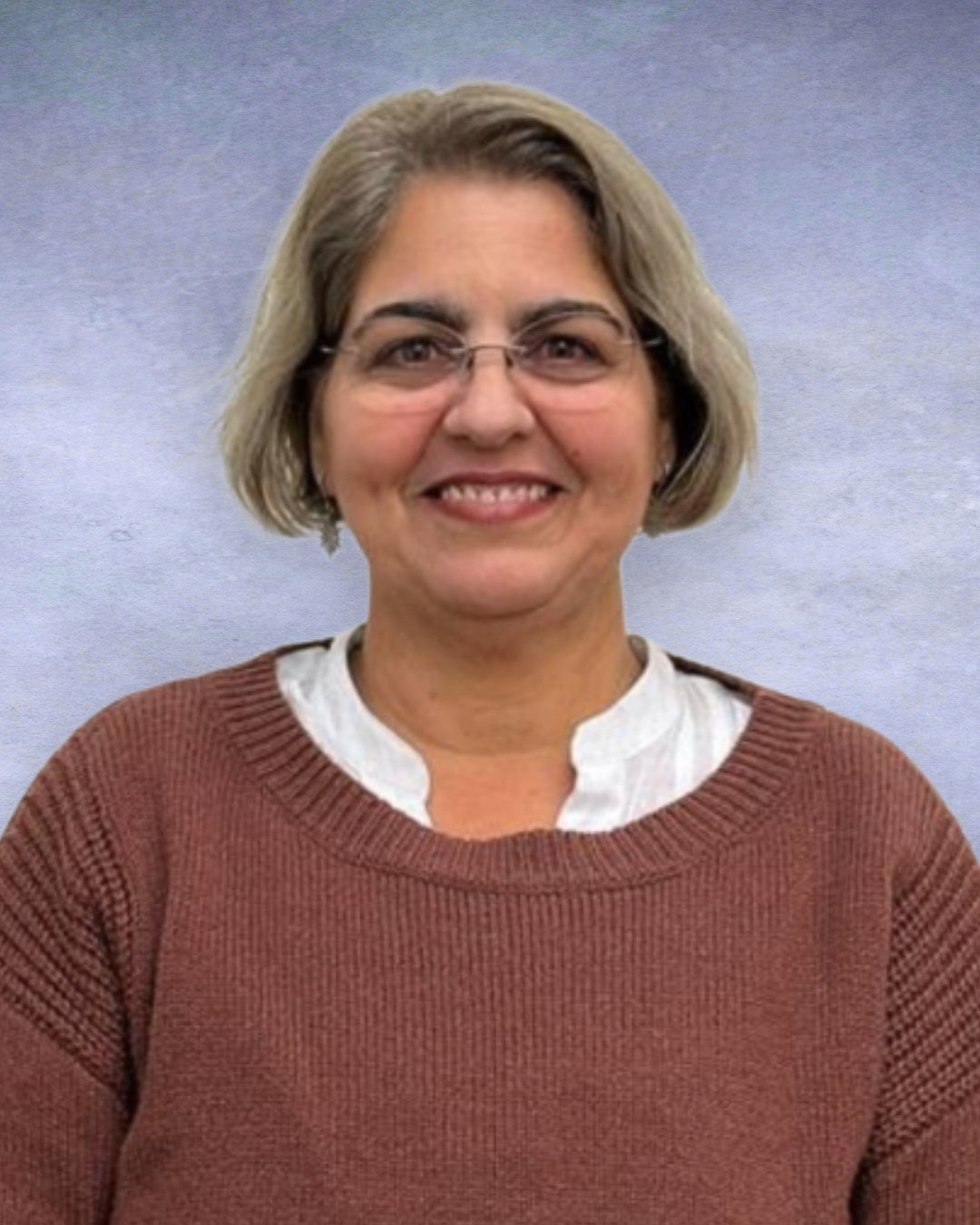 Smiling woman with glasses in a brown sweater against a soft blue background