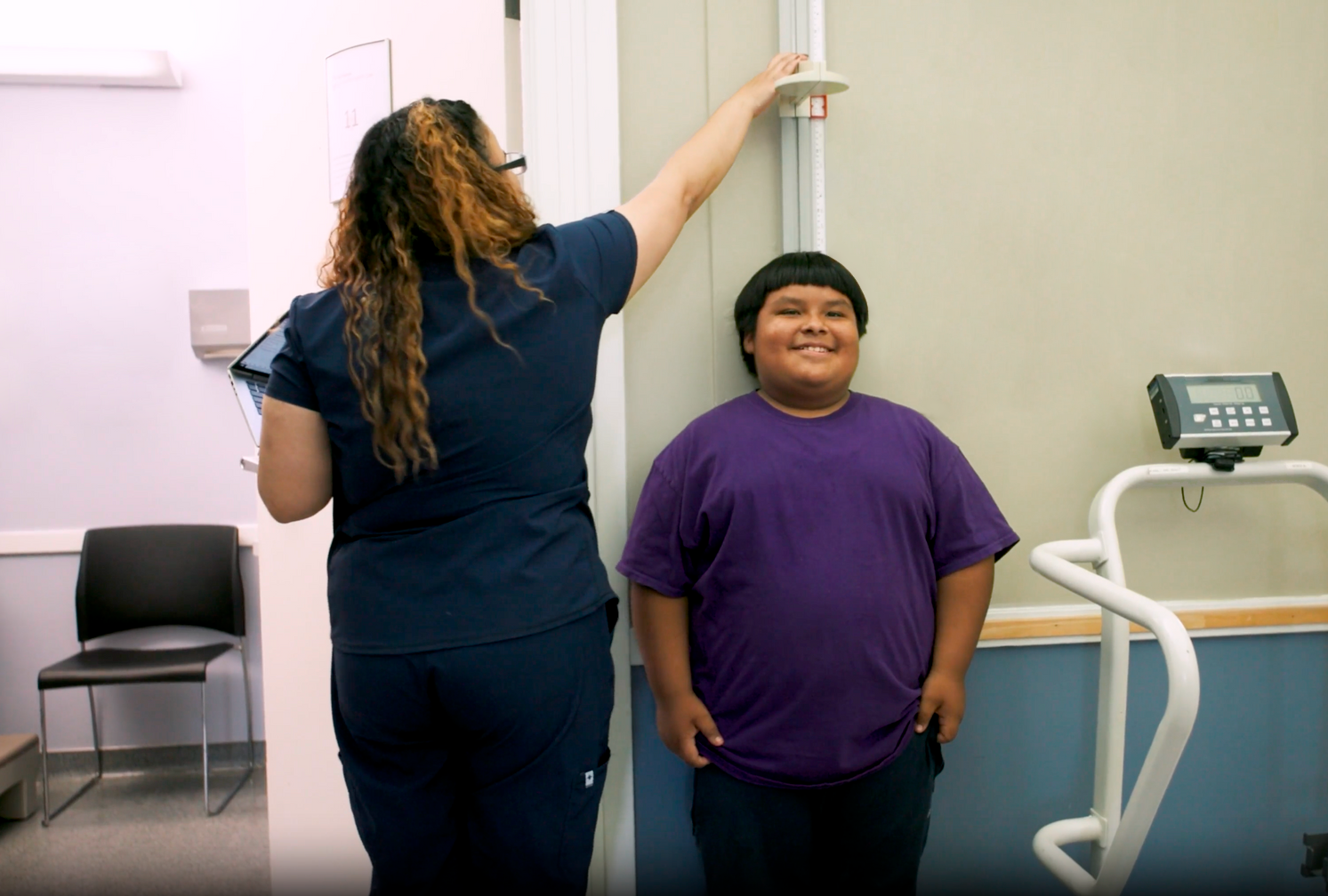 Clinician measuring a boy’s height in a medical exam room, using a wall stadiometer.