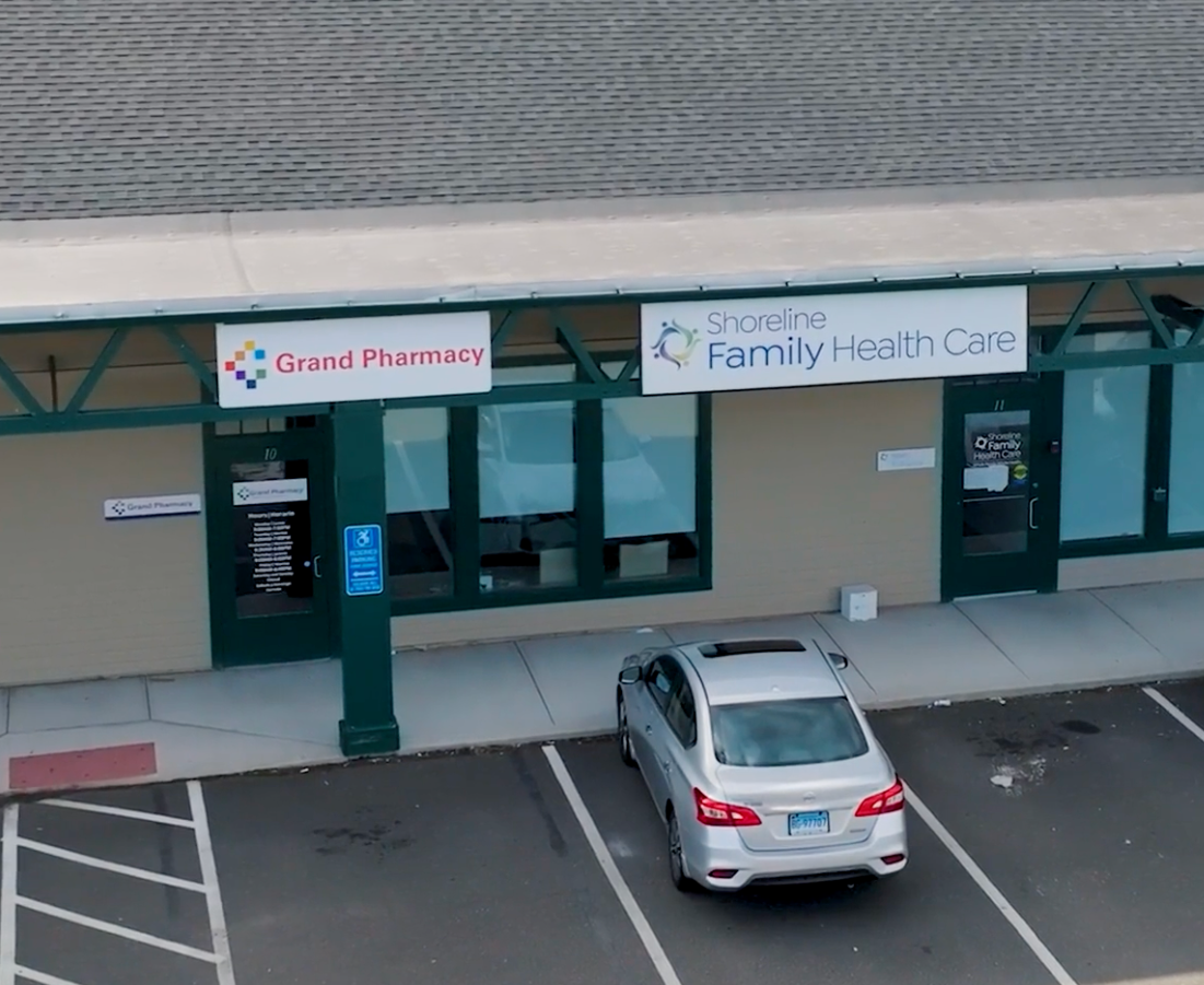 storefronts for Grand Pharmacy and Family Health Care with a silver car parked out front
