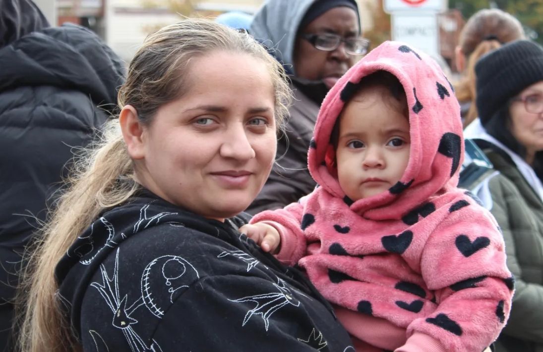Woman holding a baby in a pink heart-patterned hoodie in a crowded outdoor setting