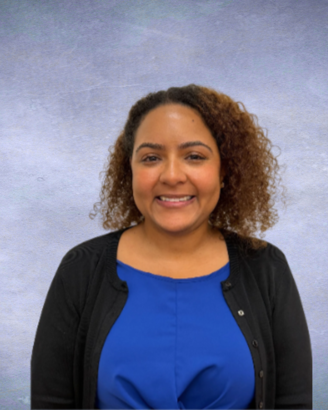 Smiling person in a blue top and black cardigan against a gray background