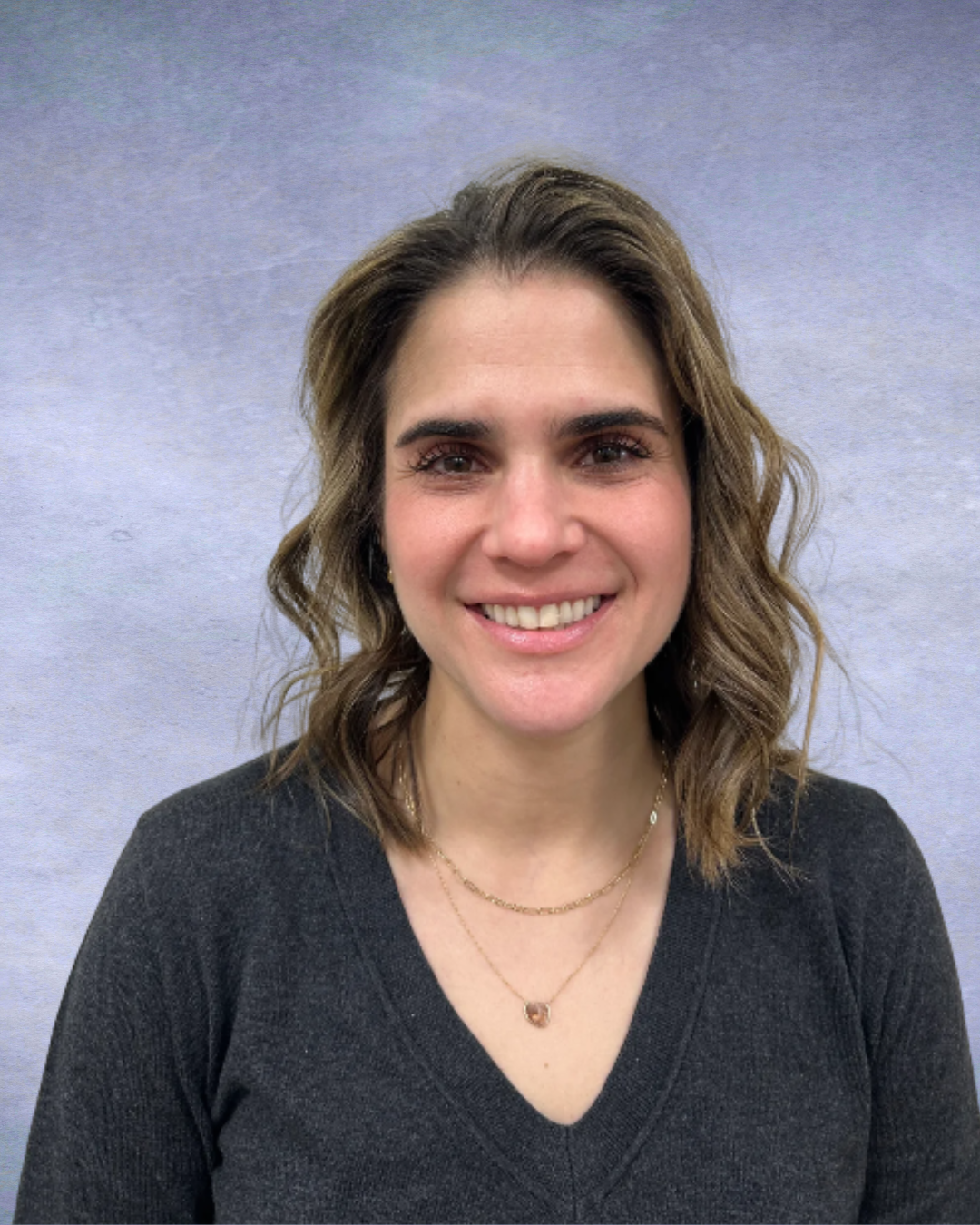 Smiling person in a dark V-neck top against a plain gray background