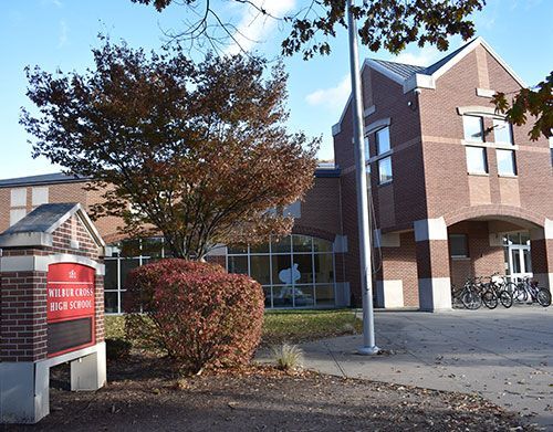 Brick building with bicycles outside, a red sign, and autumn trees on a campus walkway