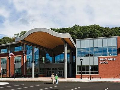 Modern school building with curved roof and glass entrance, two people walking in front