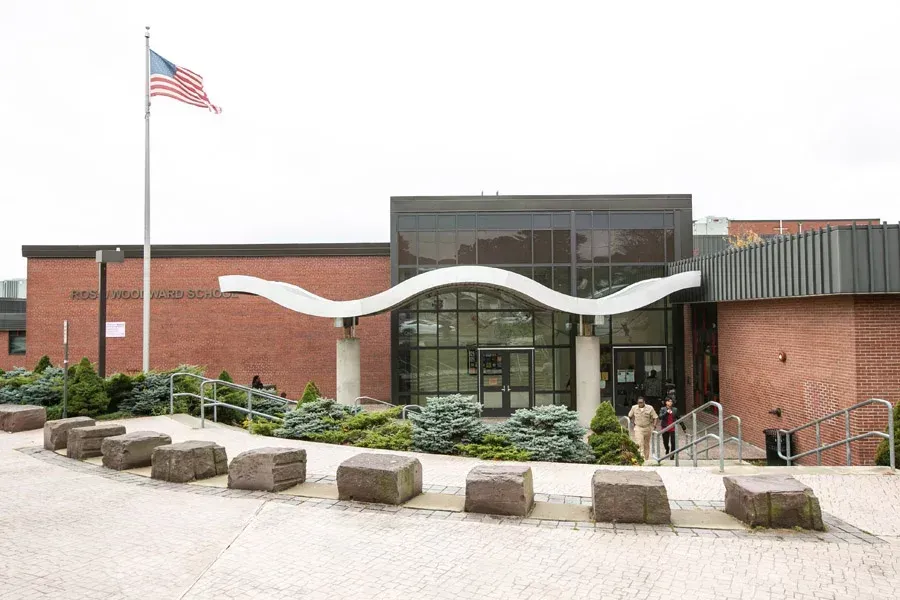 Brick civic building entrance with American flag, glass doors, and curved white sculpture on the facade