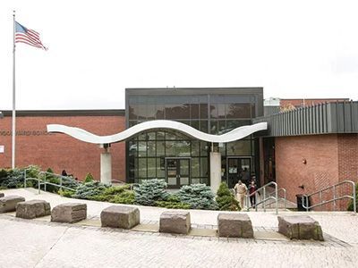 Modern brick civic building entrance with a U.S. flag, glass doors, and curved white sculpture railing