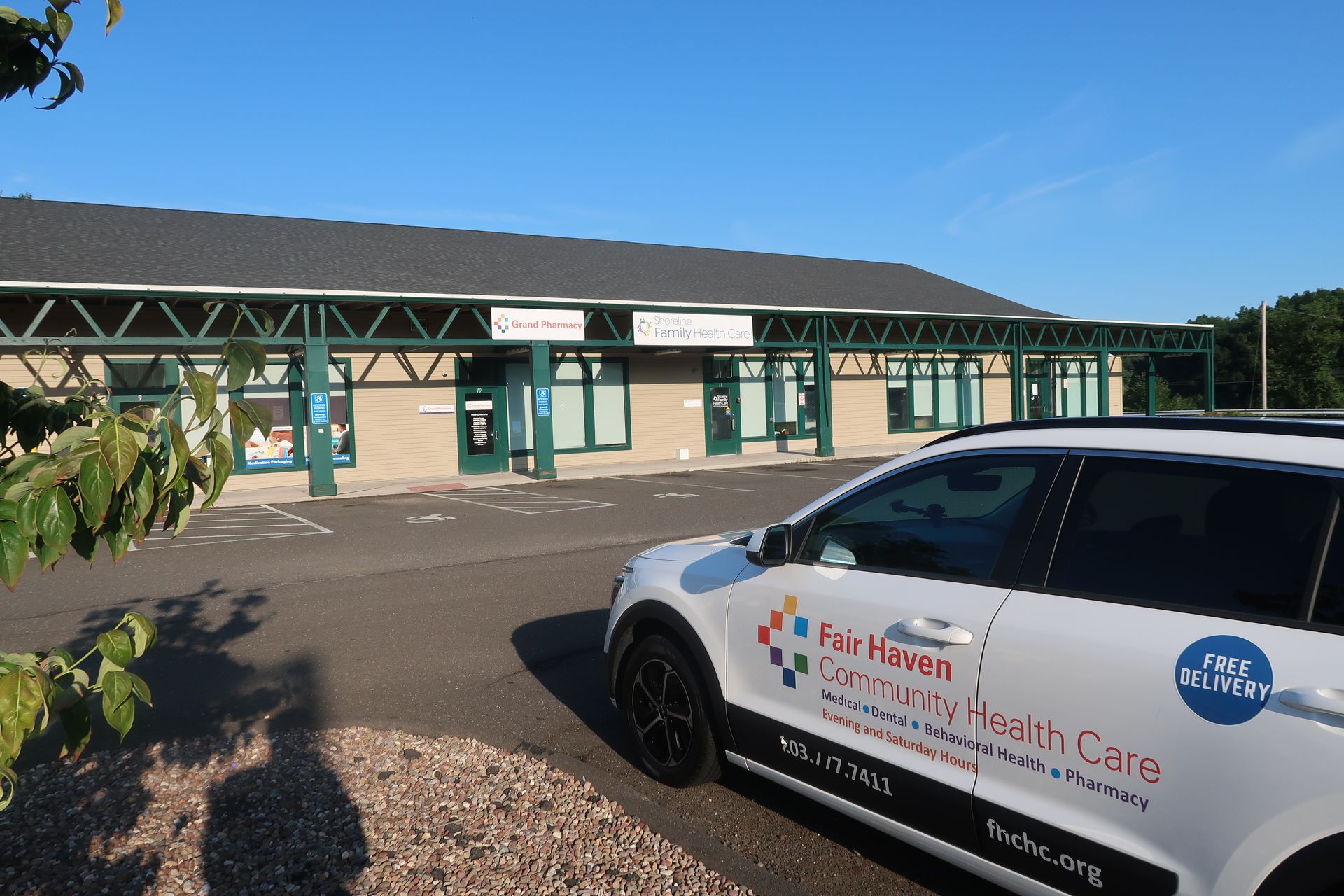 White health care vehicle parked outside a low, green-trimmed building on a sunny day