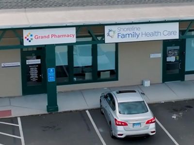 Grand Pharmacy storefront with gray facade, red sign, and colorful balloons outside