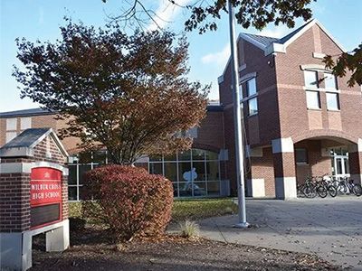 Brick building entrance with a red sign, trees, and bicycles on a sunny autumn day
