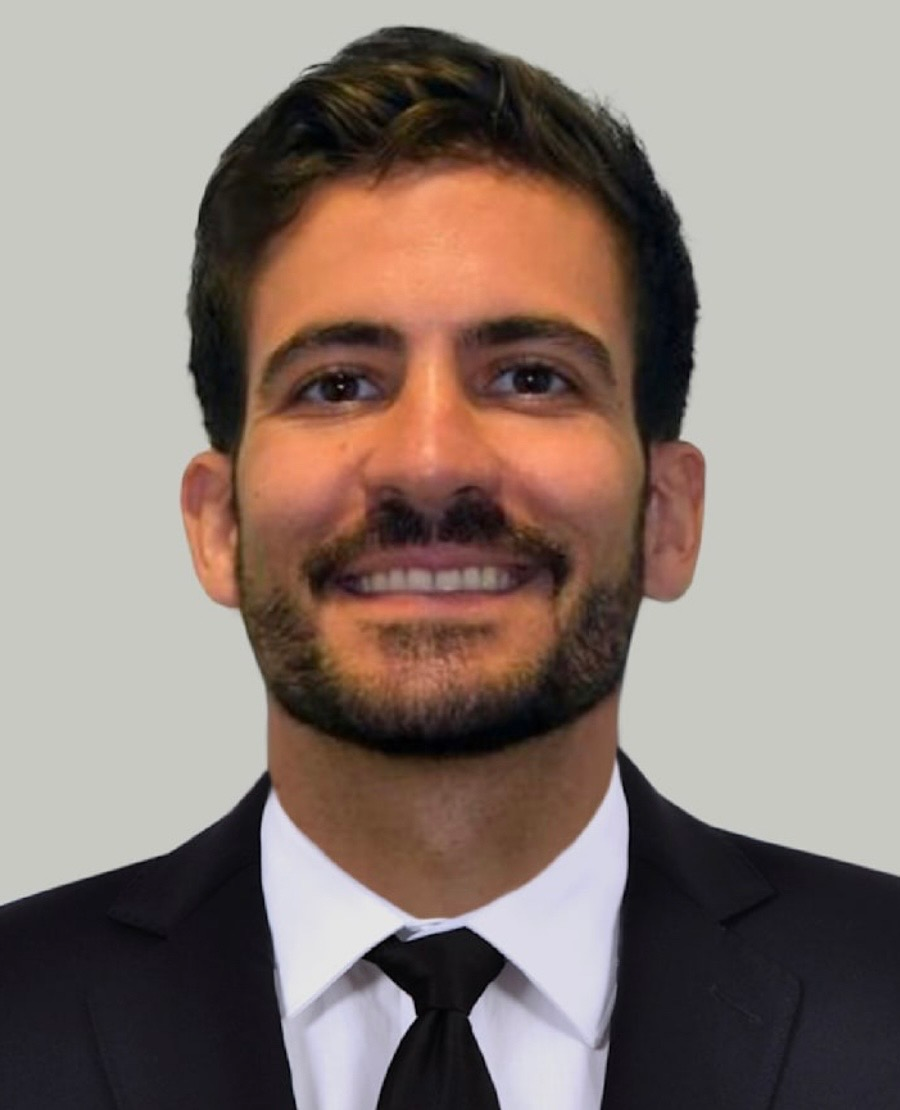 Headshot of a smiling man in a dark suit and tie against a gray background