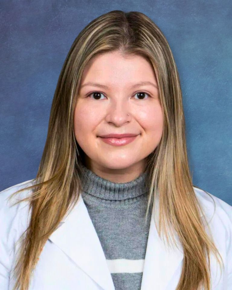 Studio portrait of a smiling person in a white coat and gray turtleneck against a blue background