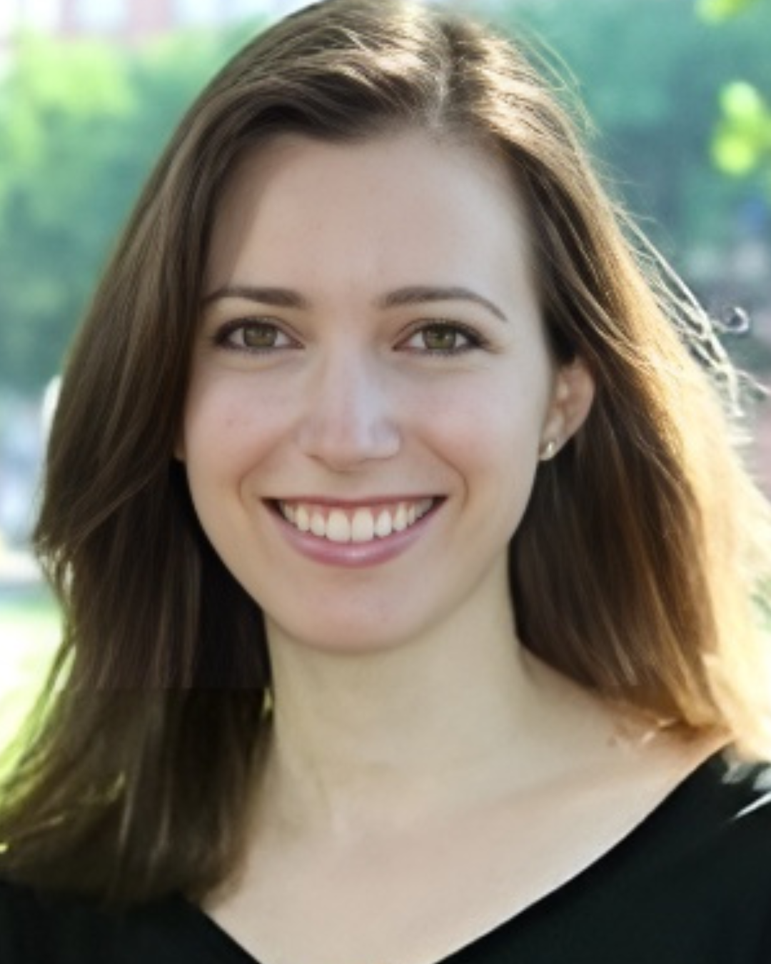 Smiling woman with shoulder-length brown hair wearing a black top outdoors with blurred greenery background