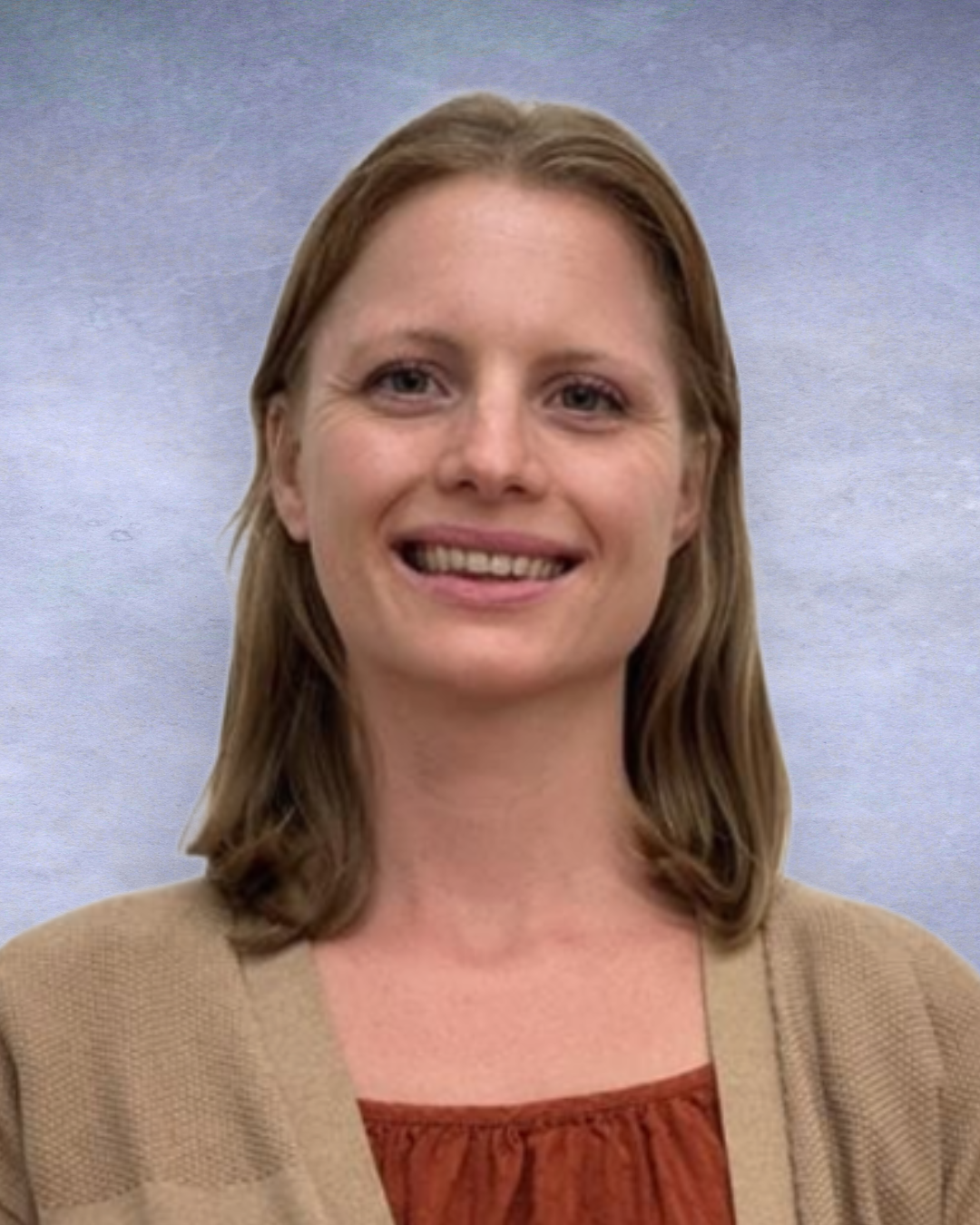 Smiling person in a beige cardigan and rust top against a soft blue-gray studio backdrop