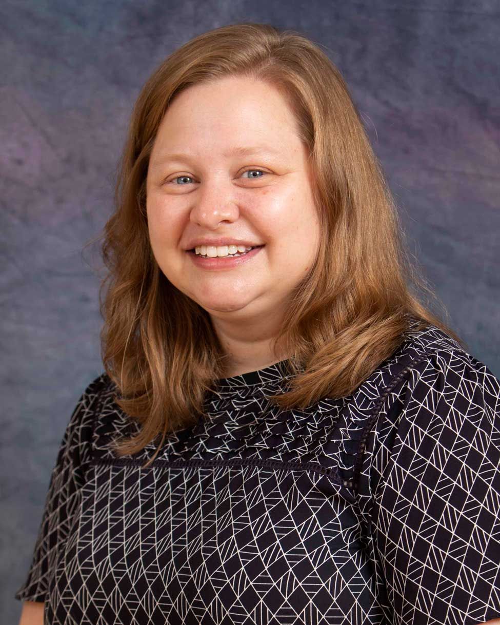 Smiling woman in a patterned black blouse against a gray studio backdrop